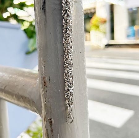 Braided stainless steel bracelet displayed on a metal surface to show its texture.