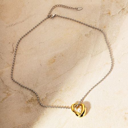 Silver chain necklace with a gold heart-shaped pendant and pearl.