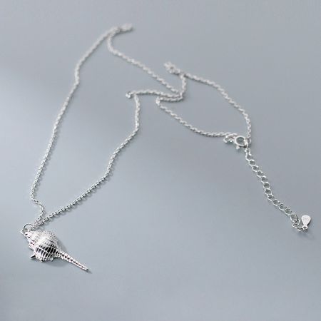 Close-up of the sterling silver conch shell necklace on a textured background.