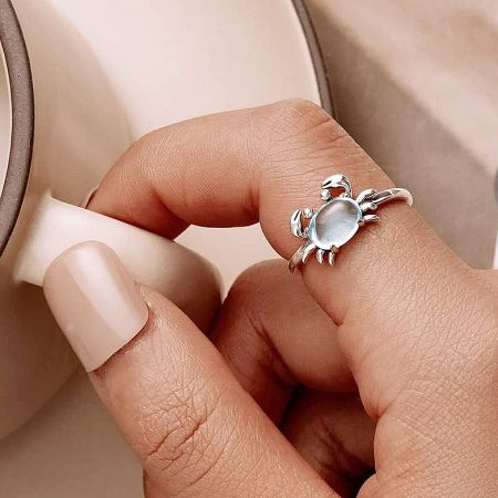 The adjustable crab ring design shown with a classic white stone, worn on a finger.