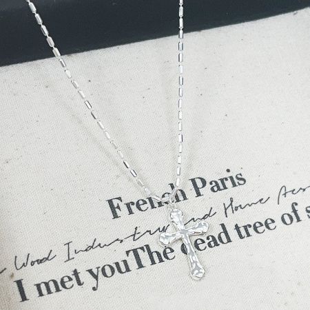 The sterling silver cross necklace displayed on a stylish fabric background for a product advertisement.