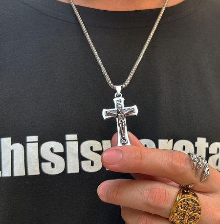Close-up of the silver cross pendant held in hand, highlighting its texture and design.