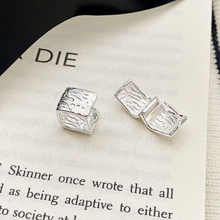 Close-up of the geometric square silver huggie earrings resting on the page of a book, highlighting their unique texture.