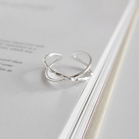 Close-up of the sterling silver crossover ring on a book, highlighting its polished finish and open ring style.