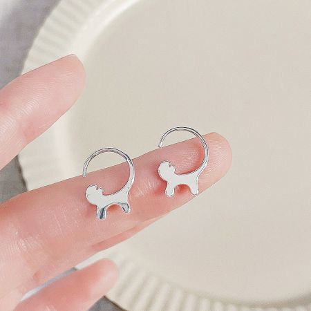 A pair of silver dog-shaped earrings held in a hand.