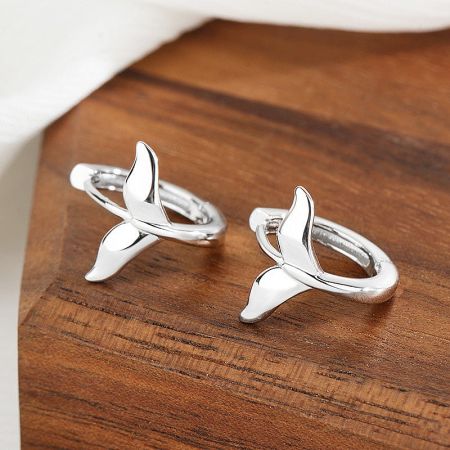 Detailed view of the intertwined whale tail design on the silver huggie earrings.