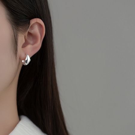Detailed close-up of a silver irregular geometric huggie hoop earring worn on an ear.