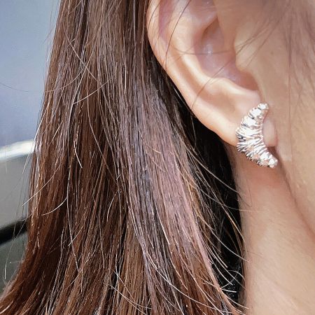 Close-up view of a sterling silver croissant stud earring being worn.
