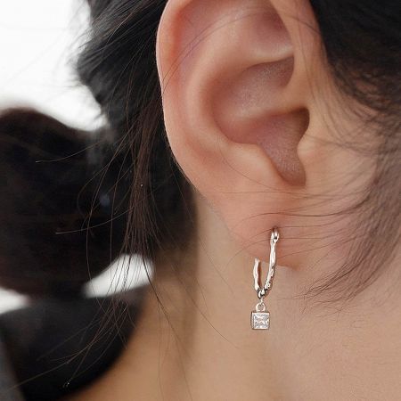 Promotional shot of the silver twisted earring with its square zircon charm.