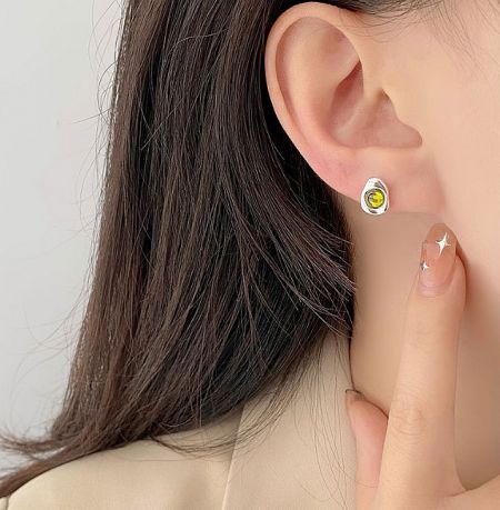 A close-up view of a woman wearing a 925 sterling silver earring with a vibrant yellow cubic zirconia stone, showcasing its sparkle and fit.
