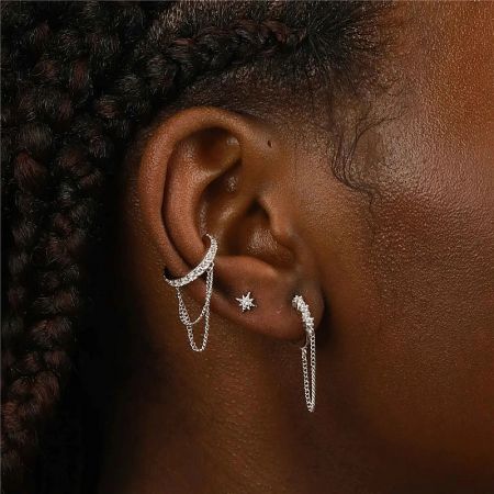A collection of silver earrings, including the chain tassel ear clip, on a model's ear.