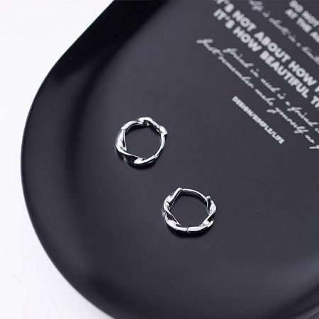 A product shot of the sterling silver twist earrings displayed on a black plate for a high-contrast view of their craftsmanship.