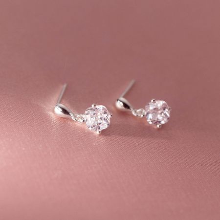 Elegant sterling silver drop earrings with cubic zirconia on a soft pink background.