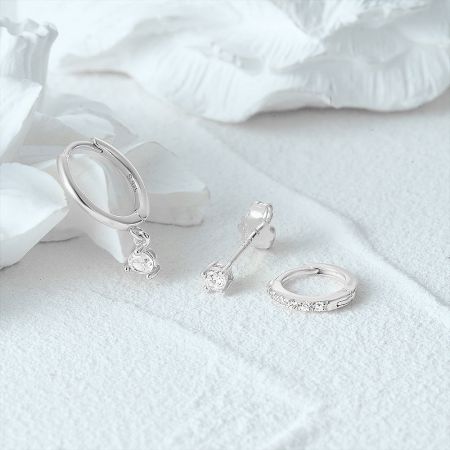 Close-up product shot of three pairs of silver zircon earrings on a white textured background.