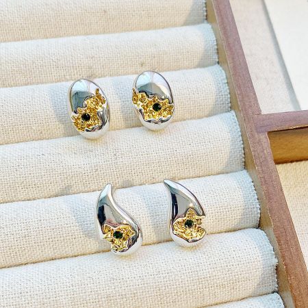 Three pairs of two-tone stud earrings with black gemstones on a wooden display.