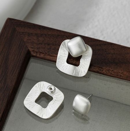 A collection of sterling silver statement earrings, including the square design, displayed on a wooden frame.