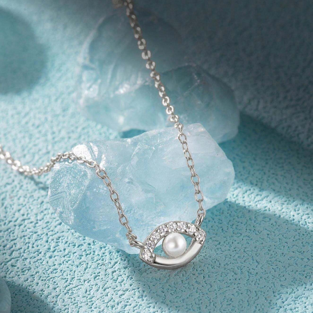 Artistic shot of the silver evil eye pendant necklace resting on a blue stone.