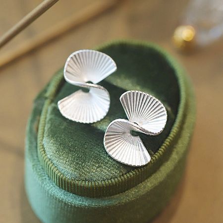 The fan-shaped silver earrings presented on a luxurious green velvet display.