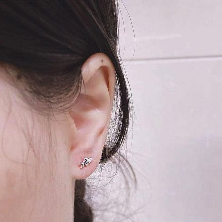 A model showcasing a tiny silver fish stud earring, illustrating its delicate size and placement on the ear.