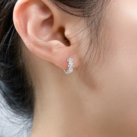 Close-up view of a sterling silver camellia flower hoop earring showcasing the intricate petal details and clear gemstones.