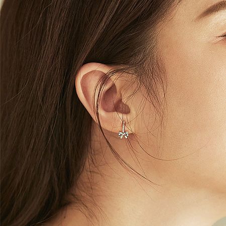 Close-up of the silver bowknot earring being worn, highlighting its delicate design.
