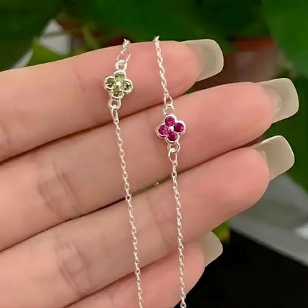Close-up of two sterling silver clover charm bracelets with pink and green stones.