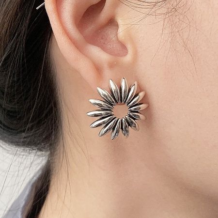 Close-up of a hollow daisy flower stud earring on a model's ear.