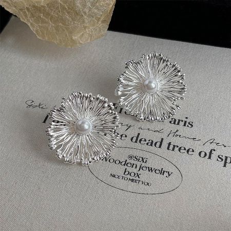 Designer style brass floral earrings with pearl centers, displayed on a neutral background.