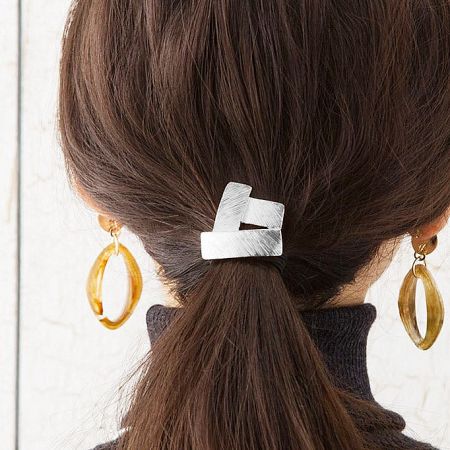 Close-up of the silver geometric stainless steel hair tie securing a woman's ponytail.