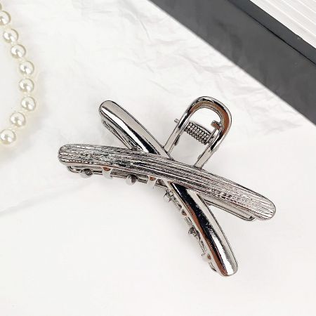 A product shot of the silver hair clip, showing its unique crossed design and textured surface.