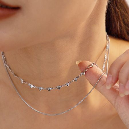 The silver version of the double-layered heart necklace worn by a model.
