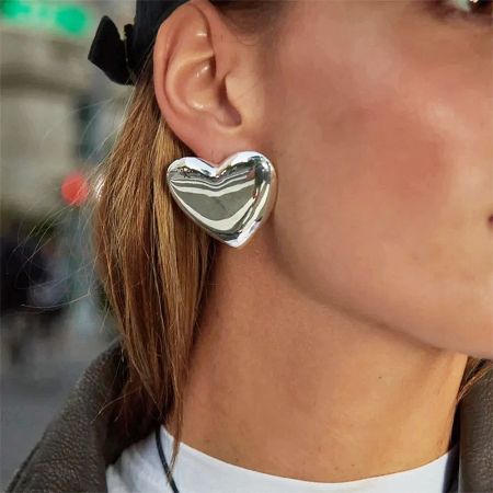 Close-up of the silver version of the heart-shaped earring on a model.