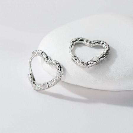 Textured silver heart hoop earrings displayed on a white stone for a stylish product view.