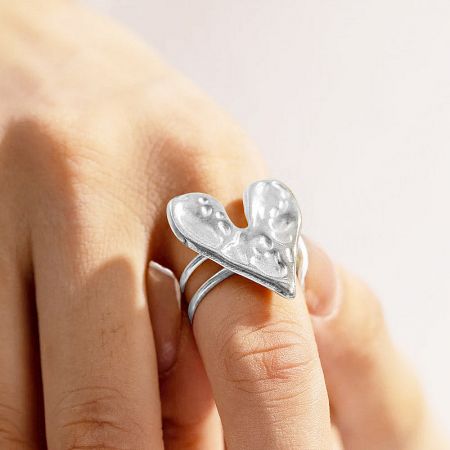 The hammered grain heart ring worn on an index finger to show its scale and style.