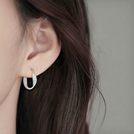 Close-up of the twisted silver huggie hoop earring being worn, showcasing its fit and shine.