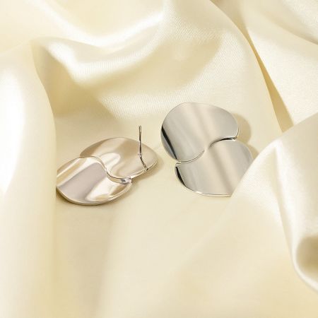 Detailed view of the silver stainless steel disc drop earrings on a satin cloth.