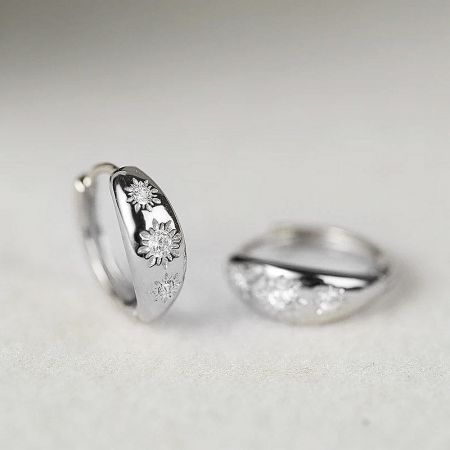 Close-up of the sterling silver CZ starburst huggie hoop earrings, showing the intricate floral and gemstone design.