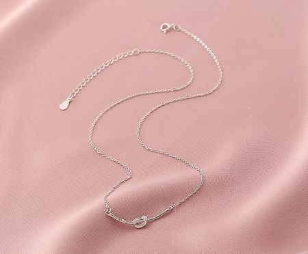 A stylish 925 sterling silver necklace with a unique knot design, displayed on a soft pink background.