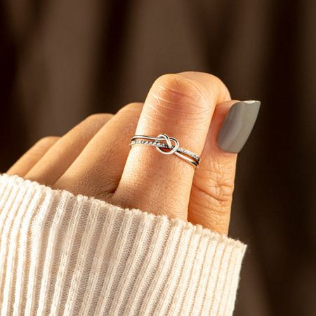 The silver knot ring with zircon accents worn on a model's index finger.