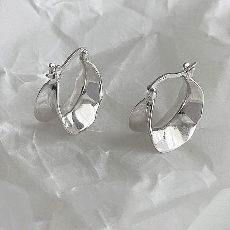Close-up of the sterling silver wide wave hoop earrings on a white textured surface.