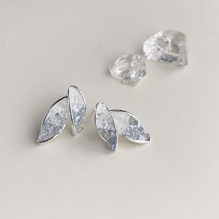 A pair of silver leaf earrings displayed with two loose clear gemstones.