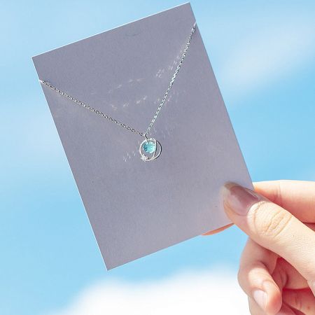 Planet pendant necklace held up against a blue sky to showcase its vibrant blue gemstone.