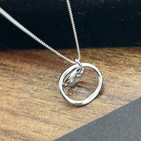 A sterling silver necklace with a unique circular pendant design against a plain background.