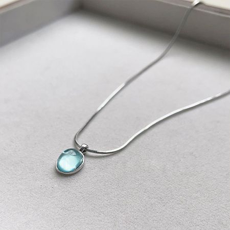 A silver necklace with a teardrop-shaped, light blue gemstone pendant.