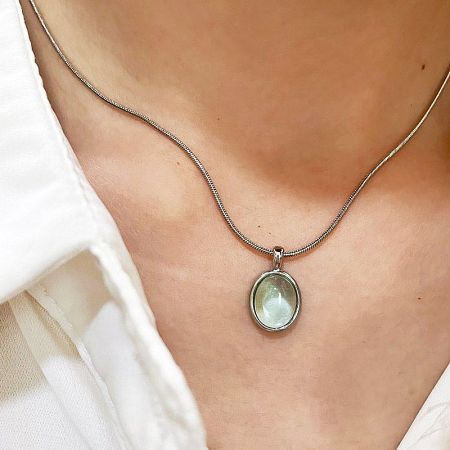 A silver necklace with a large, oval-shaped light green pendant.