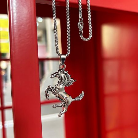 The horse pendant necklace displayed on a red background, highlighting its polished steel finish.