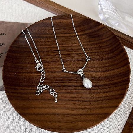Two silver necklaces with pearl pendants displayed on a wooden plate to show product variations.