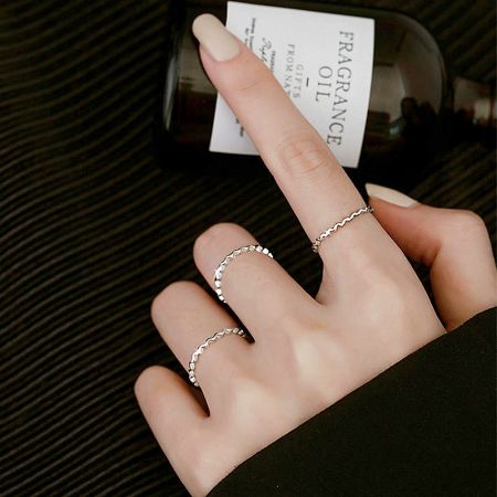 Lifestyle image of the silver waving line ring set worn on a hand, next to a bottle of fragrance oil.