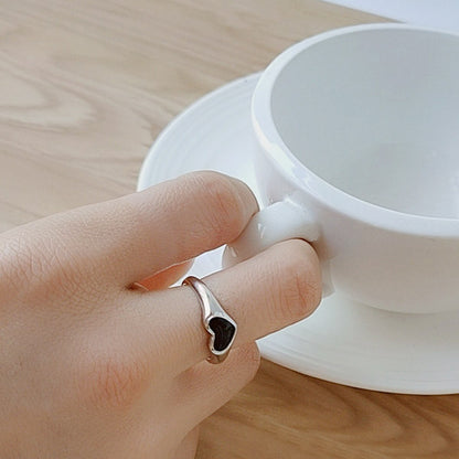 A model wearing the silver-plated black enamel heart ring while holding a teacup.