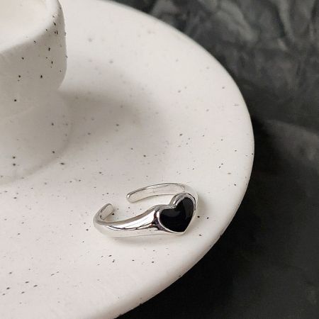 Detailed view of the black enamel heart ring on a speckled white surface.